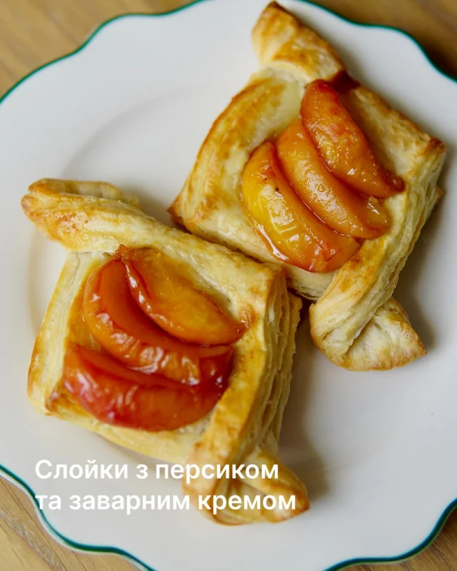 Слойки з персиками та заварним кремом 🍑

Інгредієнти:
450–500 г листкового дріжджового тіста
150 мл молока
25 г цукру
25 г вершкового масла
10 г кукурудзяного крохмалю
1 г ваніліну
1 яйце
2–3 стиглі персики
30 г шоколадного згущеного молока

Спосіб приготування:

1. У сотейнику підігрійте молоко майже до кипіння.
2. Яйце збийте та розділіть навпіл: одну частину залиште для змащування тіста, іншу змішайте з цукром і кукурудзяним крохмалем.
3. Постійно помішуючи, влийте гаряче молоко до яєчної суміші. Перелийте назад у сотейник і варіть на невеликому вогні до загустіння.
4. Зніміть крем з вогню, додайте масло та ванілін, перемішайте. Накрийте плівкою «в контакт» і залиште охолоджуватися.
5. Тісто злегка розкачайте, розріжте на 6 квадратів, сформуйте бортики та залиште на 10–15 хвилин у теплому місці.
6. Змастіть тісто яйцем, викладіть у центр крем і випікайте 10–15 хвилин при 200°C до золотистого кольору.
7. Персики наріжте скибочками та за бажанням злегка карамелізуйте з цукром.
8. На охолоджені слойки викладіть персики, додайте шоколадне згущене молоко — і готово!